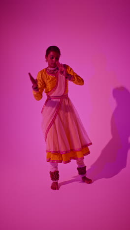 vertical video full length studio shot of female kathak dancer performing dance wearing traditional indian dress against purple background