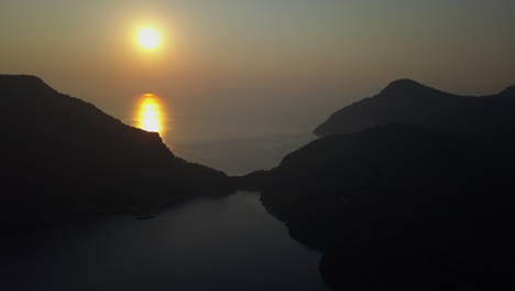 Aerial-rises-to-reveal-golden-sunset-beam-on-ocean-water-in-dark-dusk