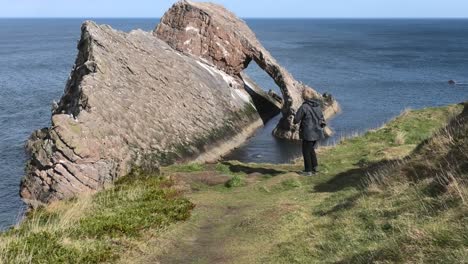 bow fiddle rock from the clifftop on a sunny calm day and a lady takes a photo