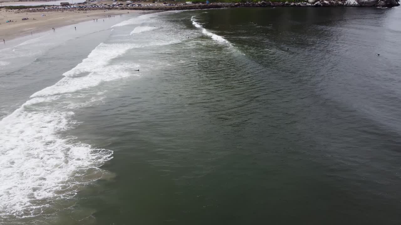 Aerial shot of waves crashing onto the sandy beach while the camera pans to reveal Morro Rock, covered in fog, and contrasted by the beach sprawling next to it. Filmed in California on a foggy day.