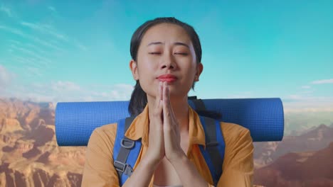 close up of asian female hiker with mountaineering backpack pray for something while traveling at the top of mountain