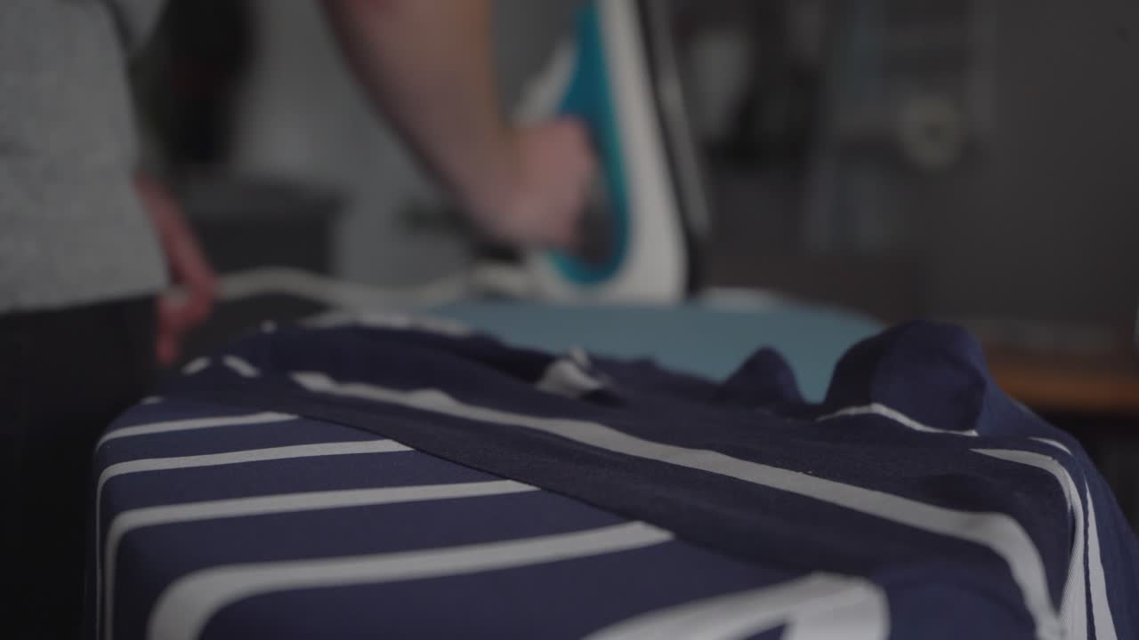 Narrow focus: Man finishes ironing striped shirt on ironing board