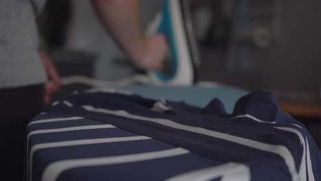 narrow focus: man finishes ironing striped shirt on ironing board