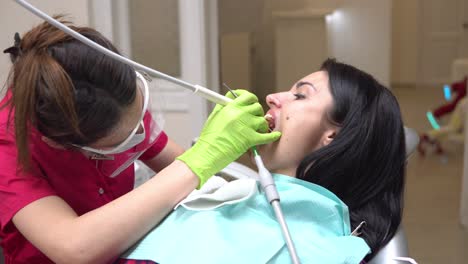 mujer en el higienista dental recibiendo blanqueamiento dental profesional y limpieza por ultrasonido. dentista usando eyector de saliva o bomba dental para evacuar saliva. filmado en 4k