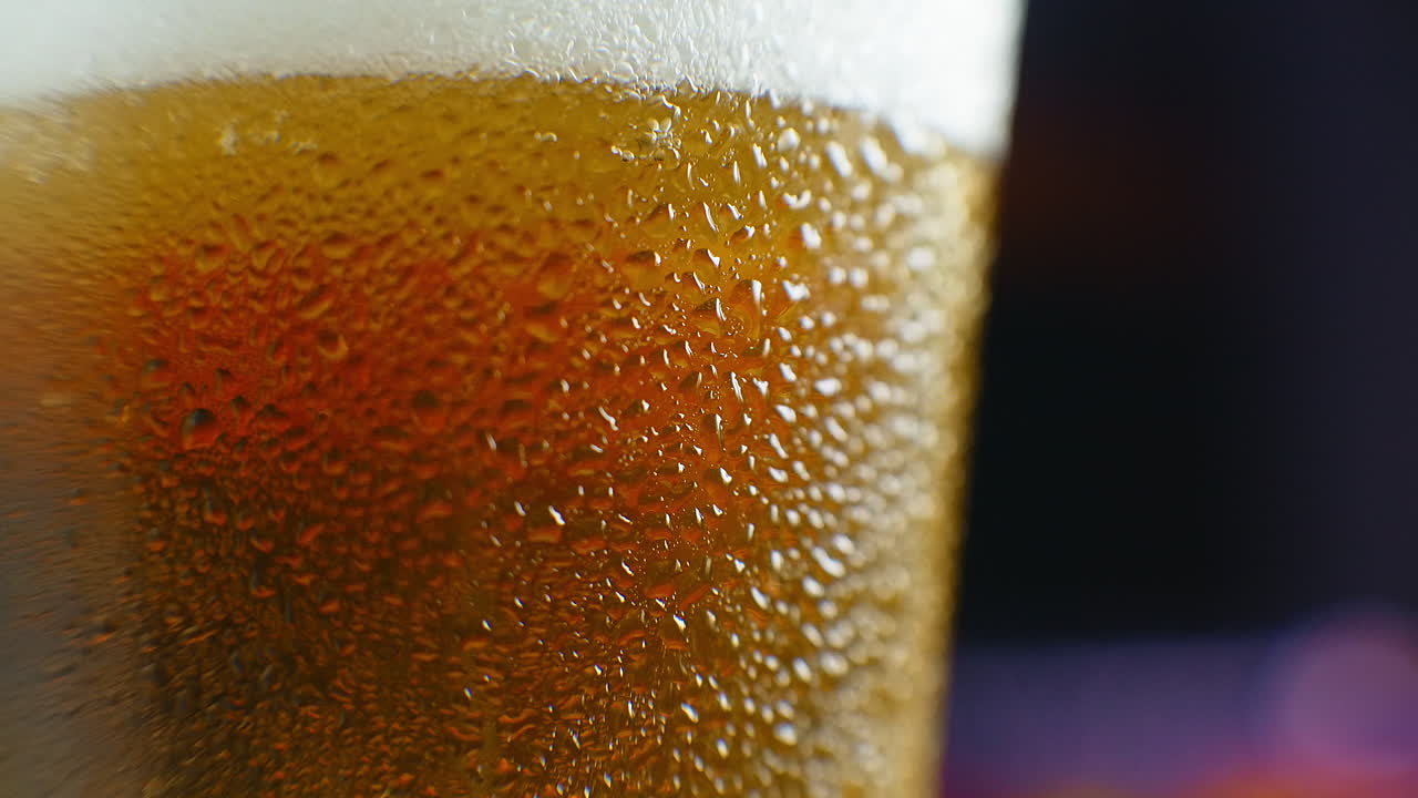 close-up cámara lenta: cerveza fría en un vaso grandes gotas y burbujas en la cerveza