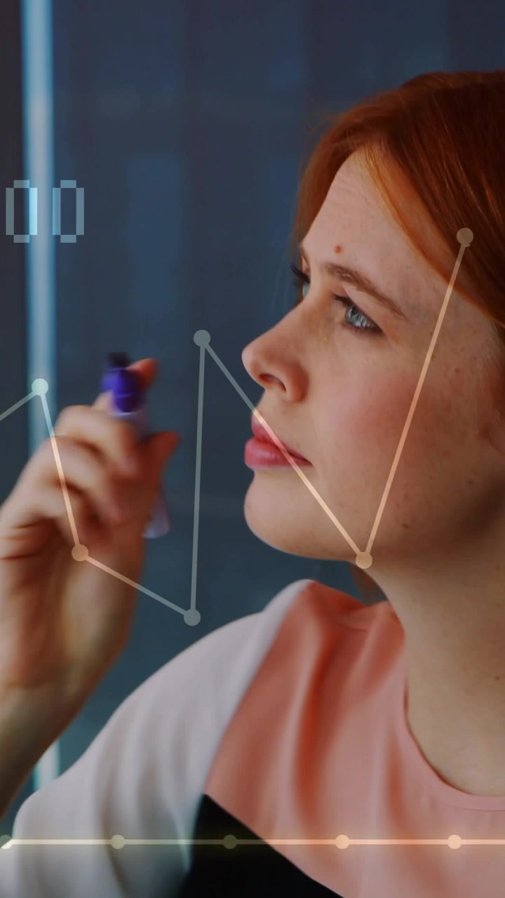 Vertical video: Woman touching purple marker assessing finance trends tracing graphs on clear board