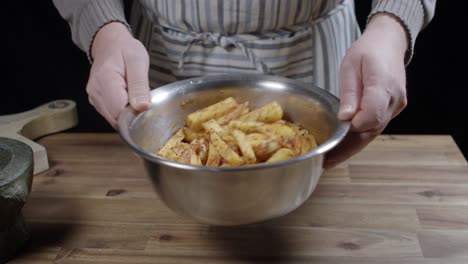 A-family-man-throws-raw-potato-wedges-into-a-metal-bowl-to-distribute-the-spices