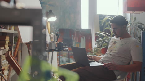 man drinking tea and using laptop in art studio