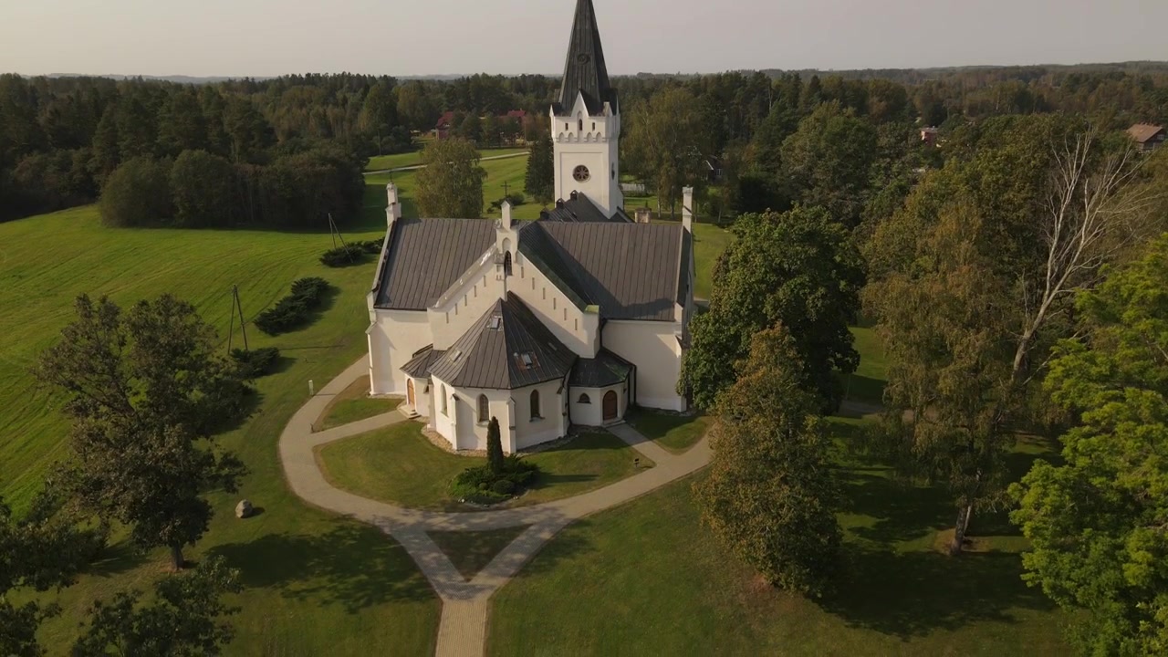 Droneutsikt over St. Thomas evangelisk-lutherske kirke i Jaunpiebalga, fanget på en lys dag. Kirken skiller seg ut blant bygningene i byen, omgitt av grøntområder og gater
