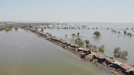 aerial flying over elevated strip of land housing makeshift tents of land surrounded by flooded landscape in mehar, pakistan