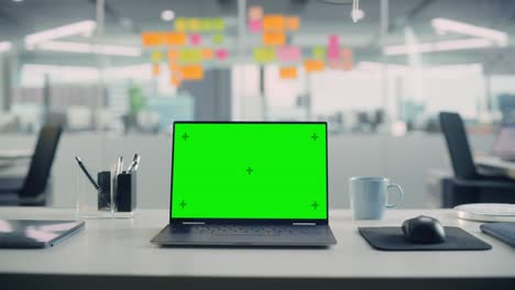 laptop computer with mock up green screen chroma key display standing on the desk in the modern creative office. in the background glass wall with colorful planning notes. zoom in shot.
