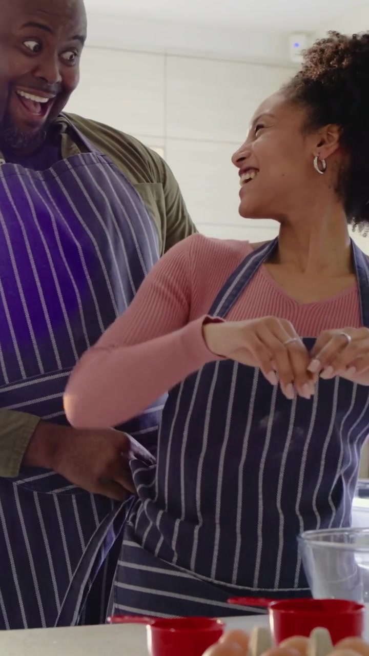 Video verticale: Uomo che si china per aiutare il partner con grembiuli a righe a rompere le uova e mescolare in cucina