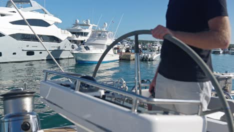 caucasian captain one hand on the helm of sailing yacht - navigating in harbor