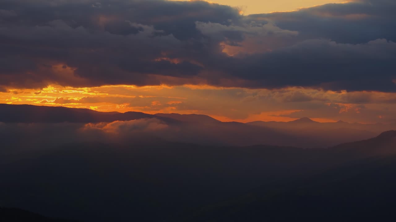 la toma panorámica revela distantes picos de montañas que surgen de un mar de niebla, bañados en la cálida luz naranja de la puesta de sol.