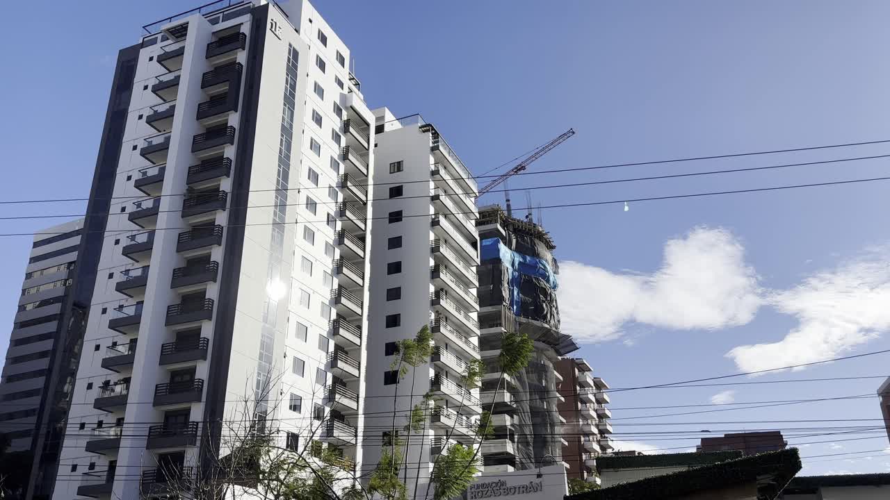 escena urbana con un edificio de apartamentos alto y moderno con una grúa de construcción y un desarrollo en curso contra un cielo azul claro