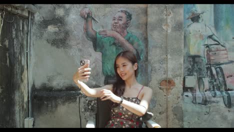 asian attractive girl takes a selfie posing in front of mural in malaysia chinatown in daytime