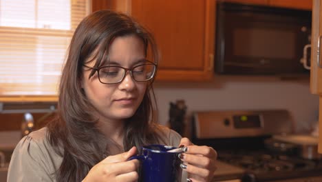 young asian mix race woman drinks cup of tea in kitchen, enjoys warm beverage