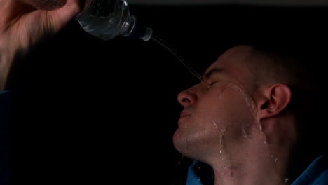 Young-man-pouring-water-from-bottle-over-face