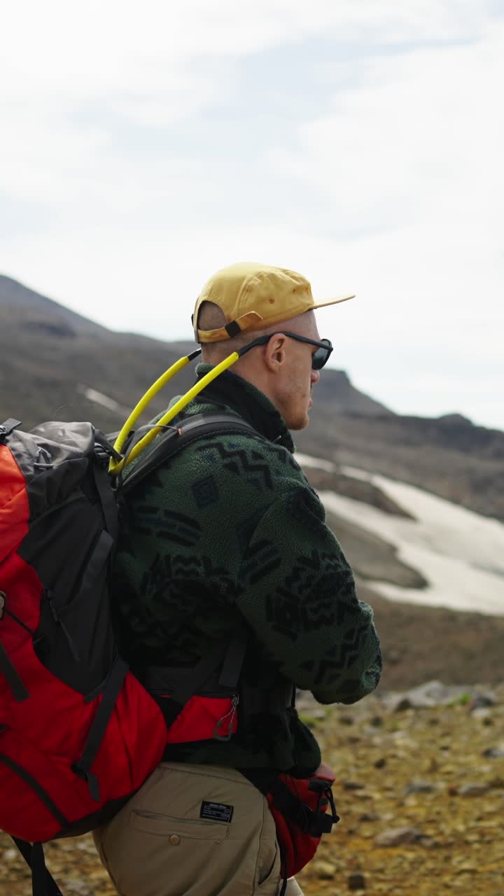 Escursionista con zaino e macchina fotografica in piedi in un paesaggio montano