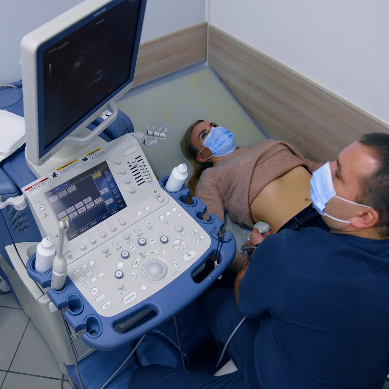 Male obstetrician applies ultrasound device to a woman's side. Doctor examines patient's kidneys. Top view