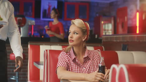 waiter serves a burger to a blonde pin up woman