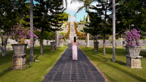 woman walking on a path towards a grand staircase in a lush tropical garden