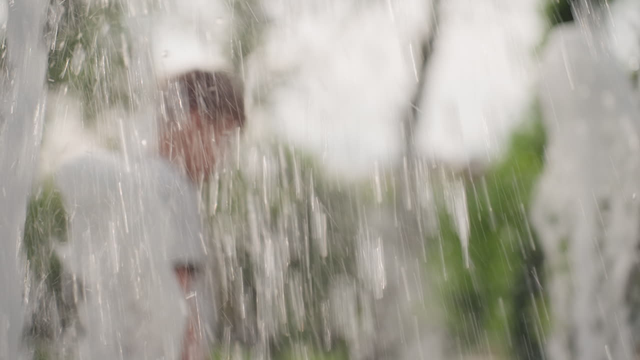 young playmates touching and playing with water from fountain in park, summer laughter and splashes, blurred background greenery, joyful energy and curiosity of children exploring cool droplets