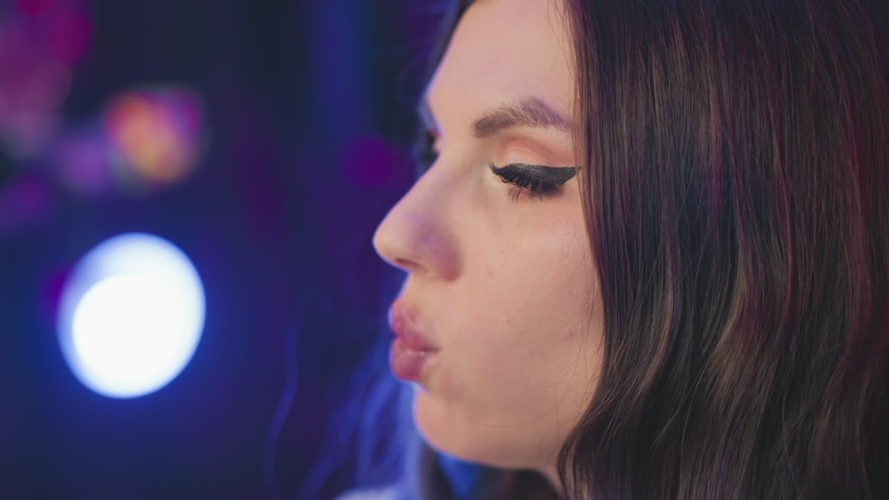 Close up of girl eating popcorn with fingers near lips, adjusting her hair slightly while illuminated by soft moody lights in cozy studio setup with colorful blurred background