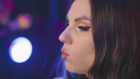 close up of girl eating popcorn with fingers near lips, adjusting her hair slightly while illuminated by soft moody lights in cozy studio setup with colorful blurred background