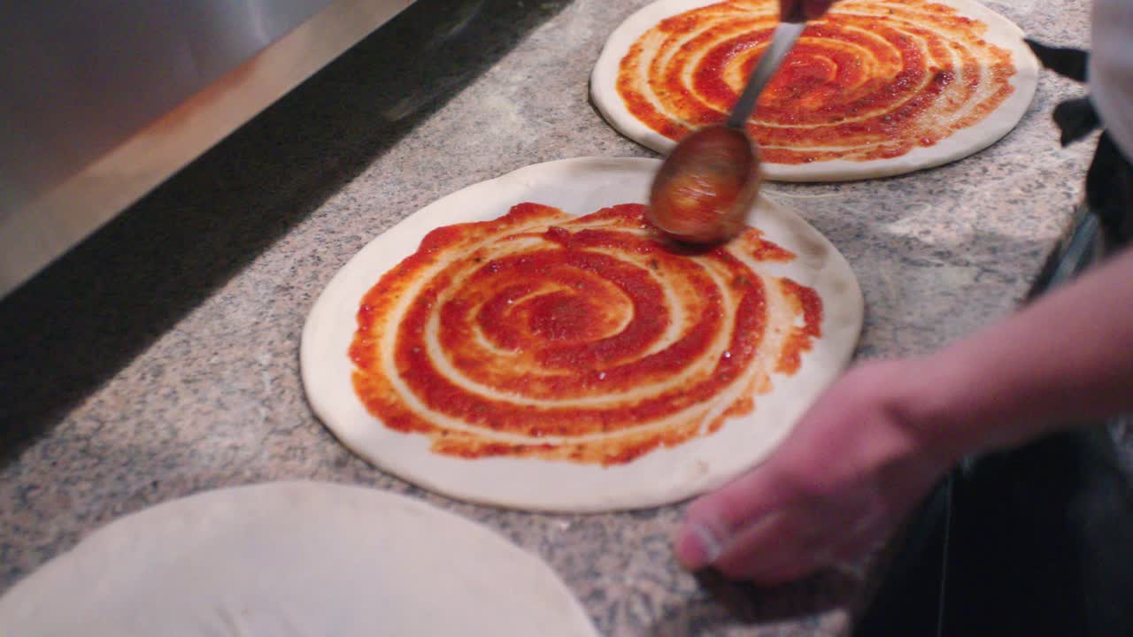 요리사는 피자 반죽에 신선한 토마토 소스를 퍼뜨립니다.