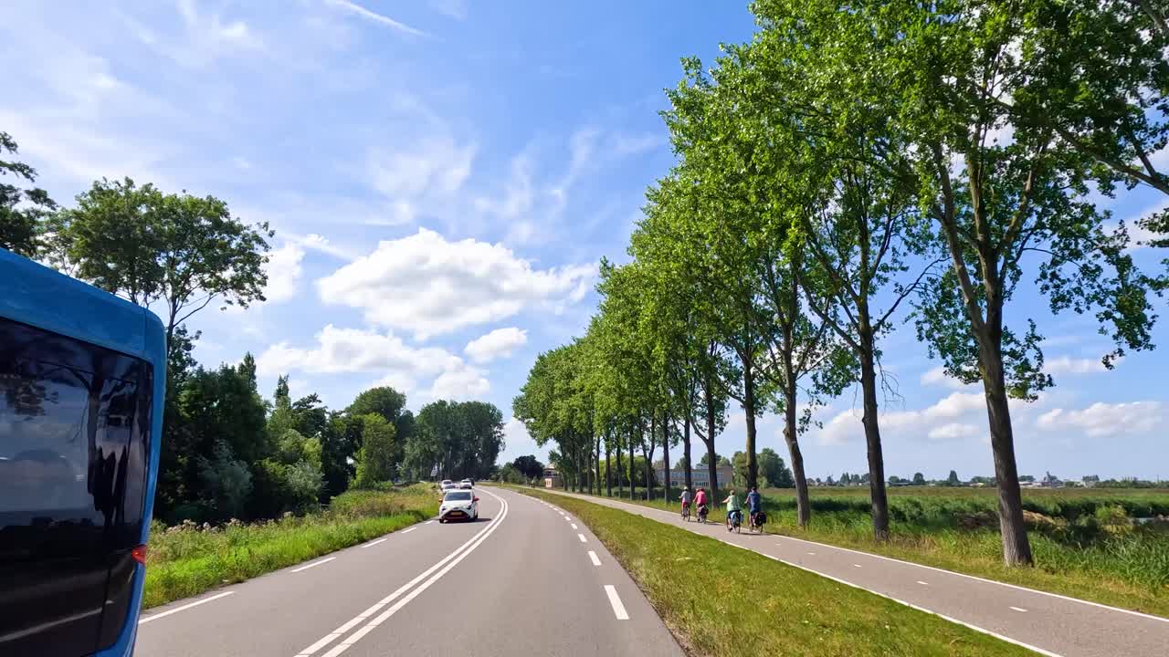 Sunny summer drive along rural Dutch road with cyclists, cars, bus, greenery, and blue sky