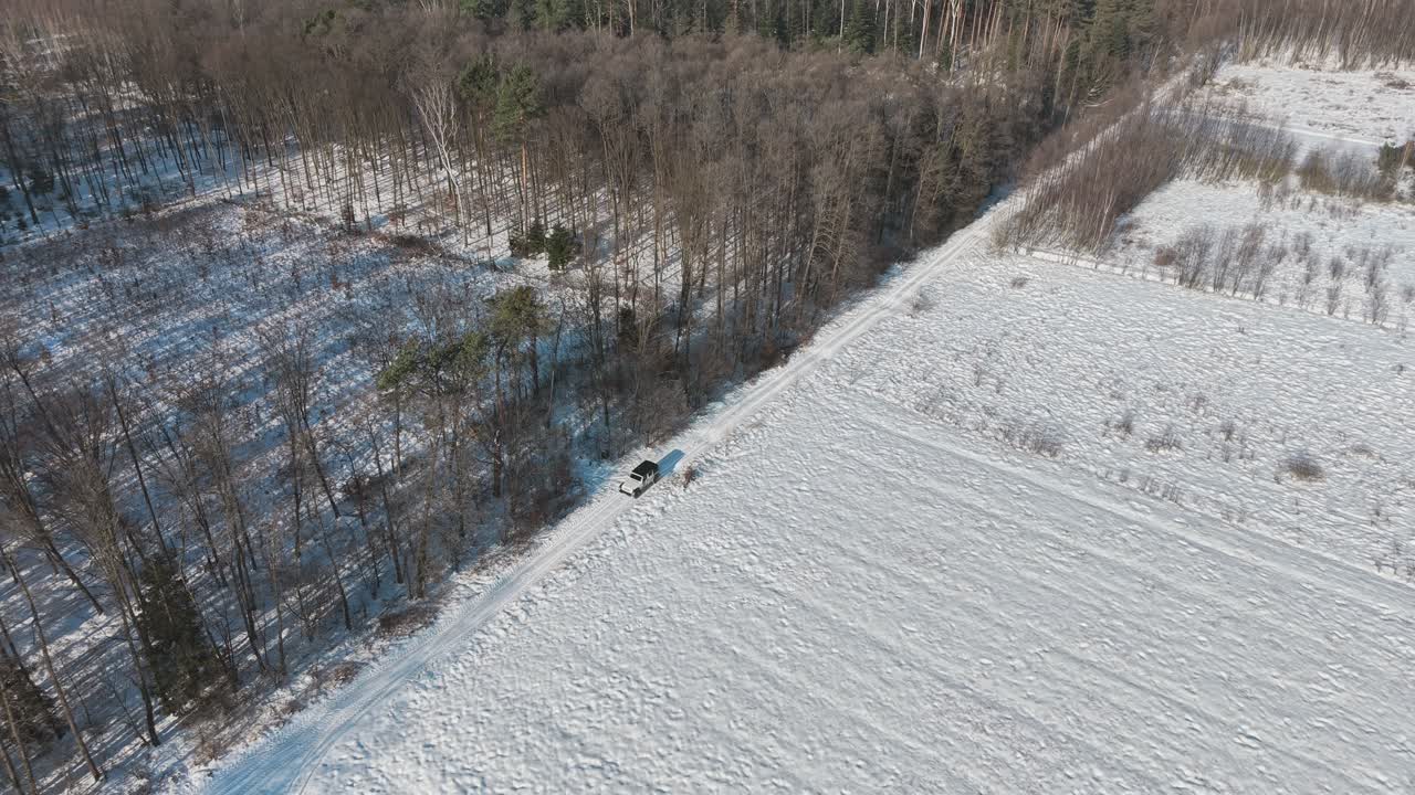 Vista aerea di una jeep che guida lungo il bordo di una foresta innevata nella Polonia rurale, mostrando la campagna invernale, i viaggi d'avventura, l'esplorazione della natura e paesaggi remoti