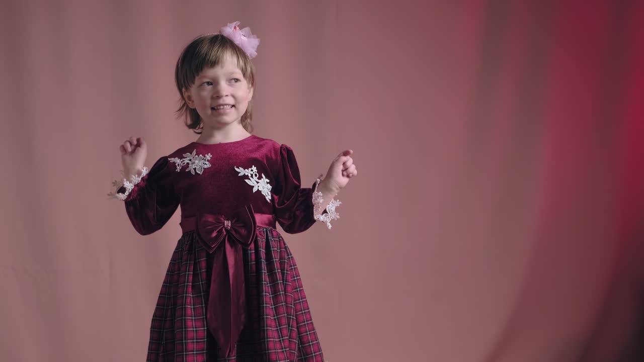Little girl in vintage burgundy dress is dancing, rejoicing, making funny faces