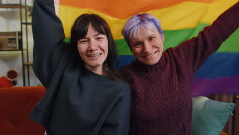 two women holding a rainbow pride flag, smiling and looking at the camera