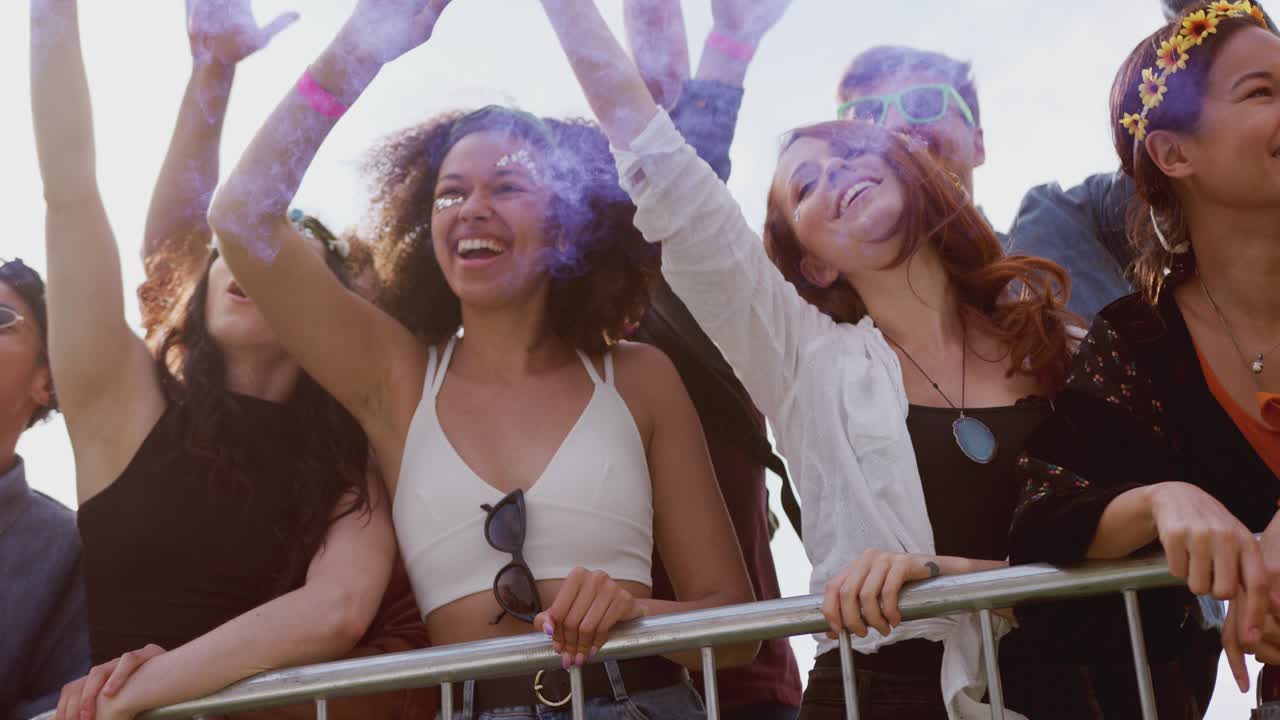 Group of young friends dancing behind barriers at music festival site with smoke flare - shot in slow motion