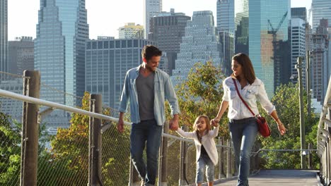 Young-couple-and-daughter-walking-on-footbridge-in-Manhattan
