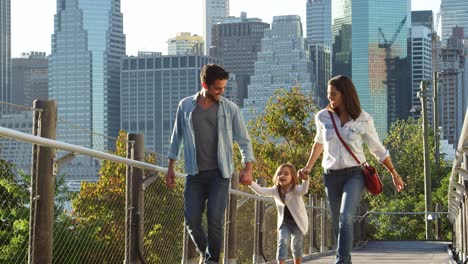 young couple and daughter walking on footbridge in manhattan