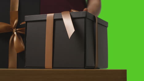 Close-Up-Of-Man-Picking-Up-Gift-Wrapped-Present-In-Box-Decorated-With-Ribbon-On-Table-Shot-Against-Green-Screen