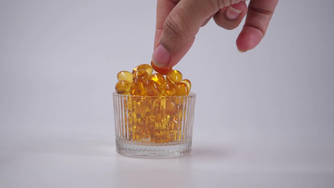Mano che raccoglie capsule vitaminiche gialle a forma di cuore da un contenitore di vetro
