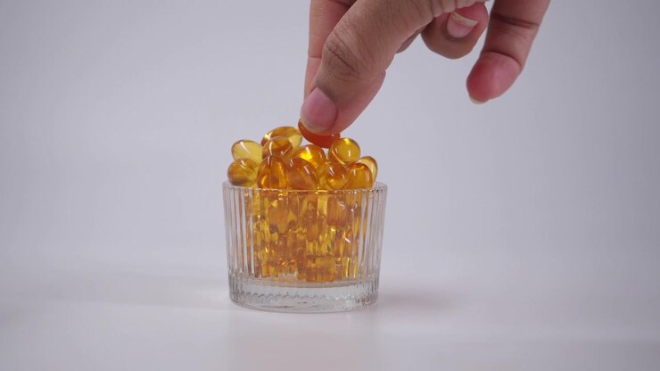 Mano che raccoglie capsule vitaminiche gialle a forma di cuore da un contenitore di vetro