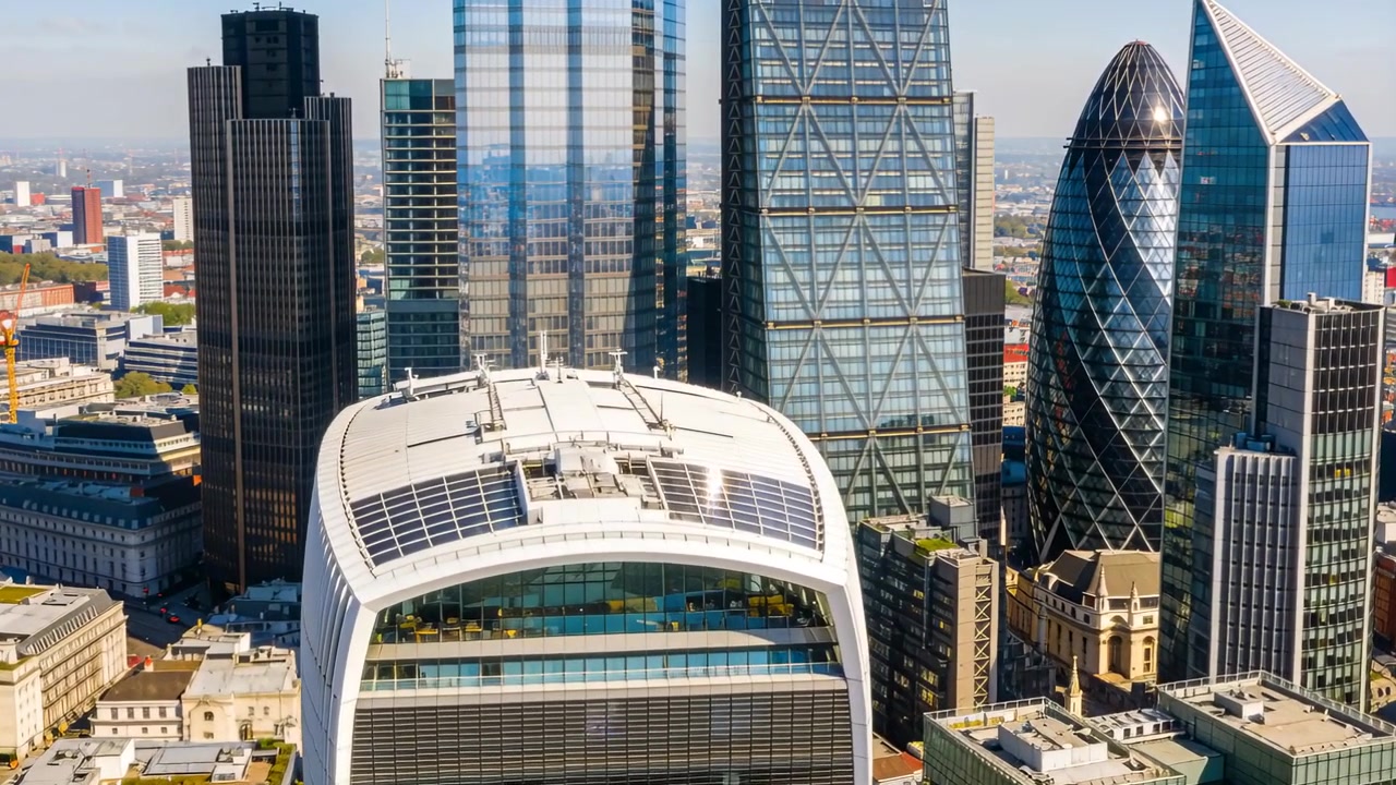 Un drone in movimento rivela una torre bianca curva, pannelli solari e un sistema HVAC sul centro città mentre si avvicina.