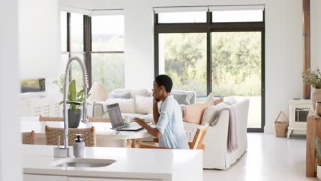 happy african american woman sitting at table talking on smartphone and using laptop, slow motion
