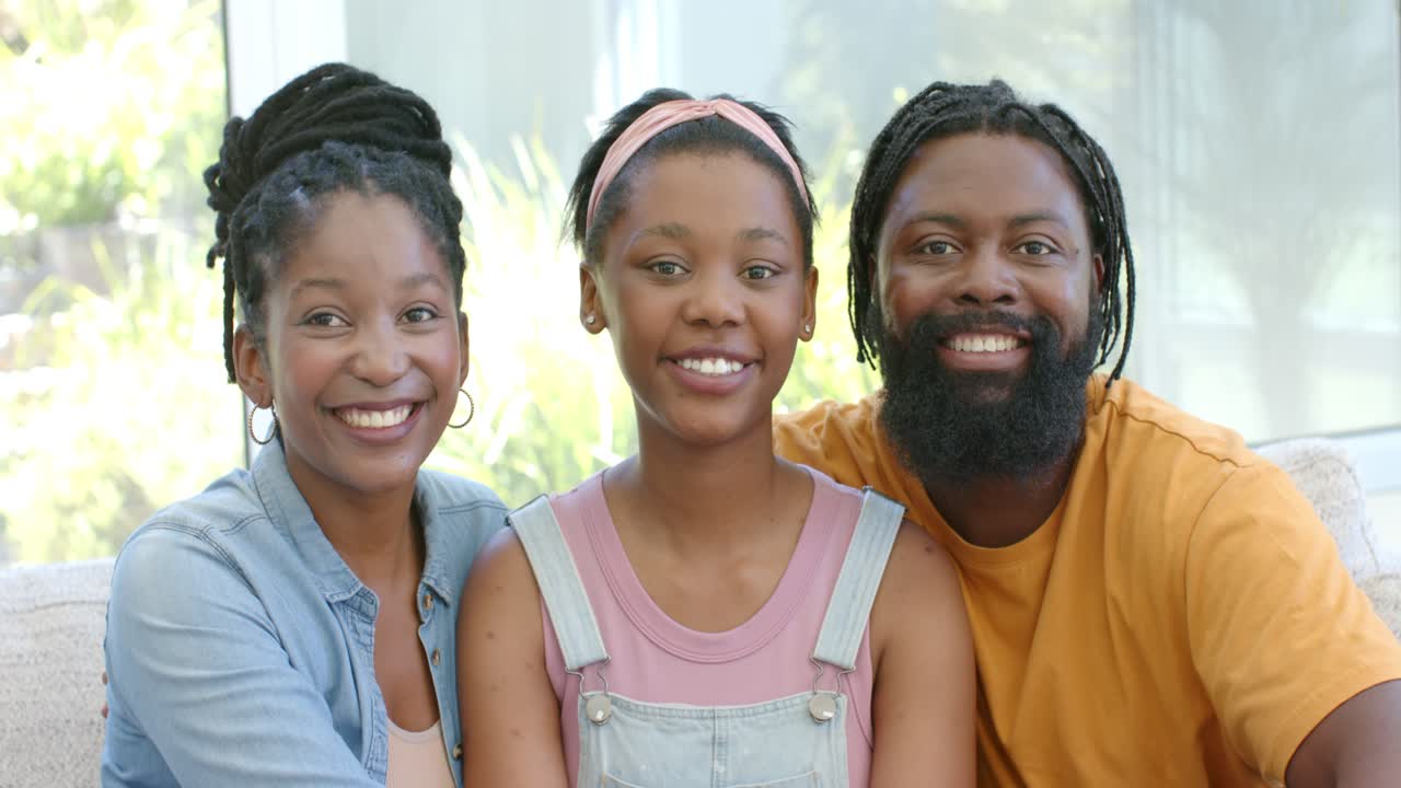 African American family posing for camera on light sofa by window, smiling and leaning for portrait