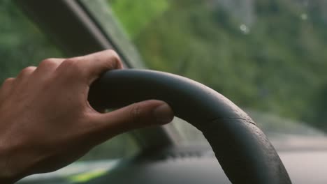 Close-up-of-a-hand-of-a-person-driving-and-using-the-steering-wheel-of-a-car,-traveling-background