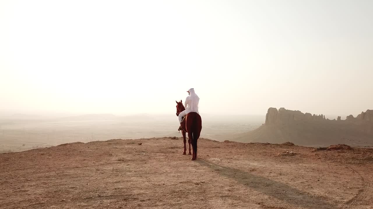 Arabian horseman gazing enless desert horizon from high plateau, dolly in shot