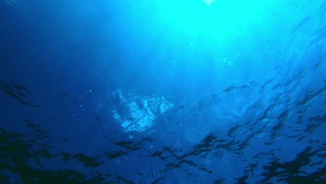 Underwater-shot-of-the-surface-of-the-ocean-with-rays-of-sunlight-punching-through-the-many-nuances-of-blue