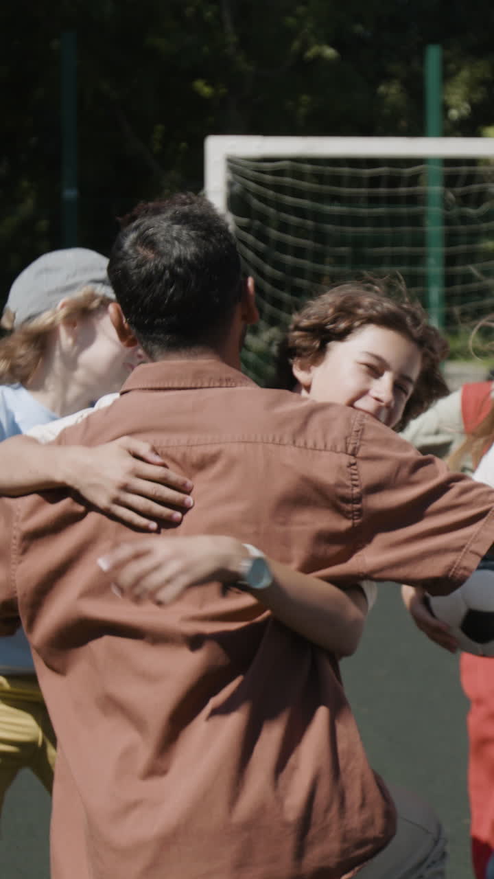 Children joyfully embrace a man in a group hug on a sports field