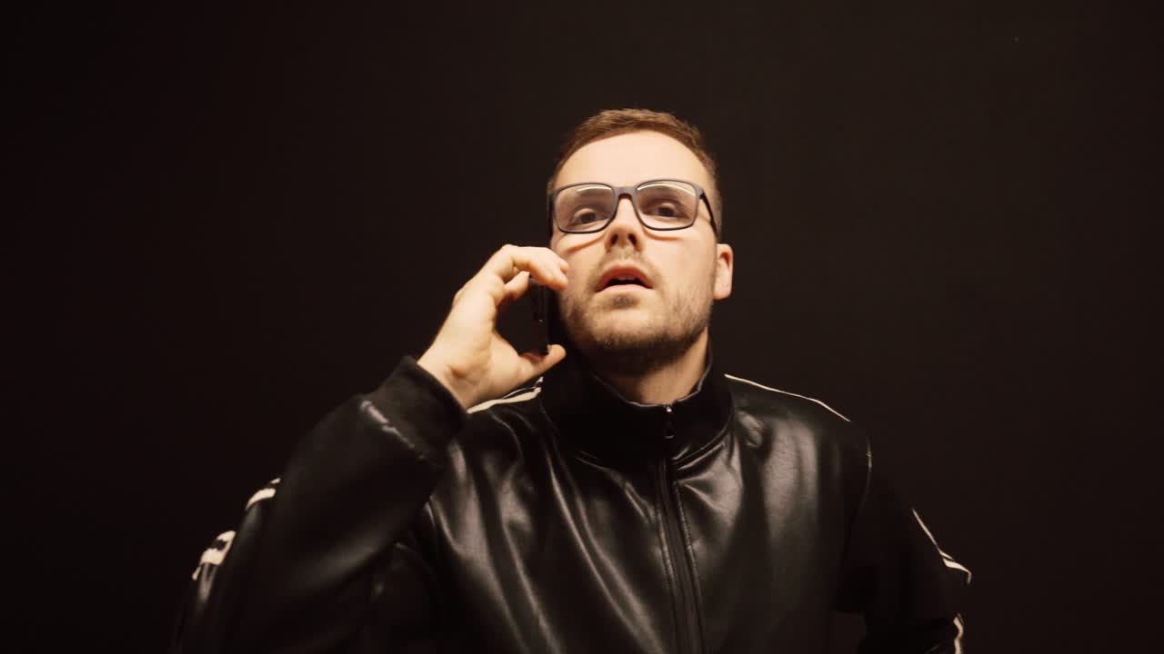Mezzo busto di un uomo che parla su uno smartphone con gesti espressivi delle mani su uno sfondo scuro. Concetto di comunicazione, chiamata di lavoro, discussione, negoziazione e uso della tecnologia moderna.