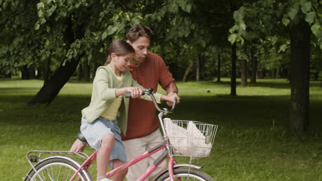 father teaching daughter to ride bicycle in park