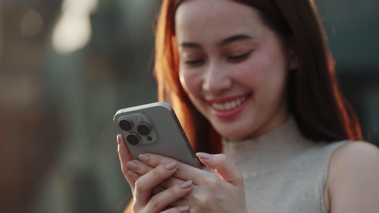 Giovane donna asiatica felice che sorride mentre usa lo smartphone all'aperto